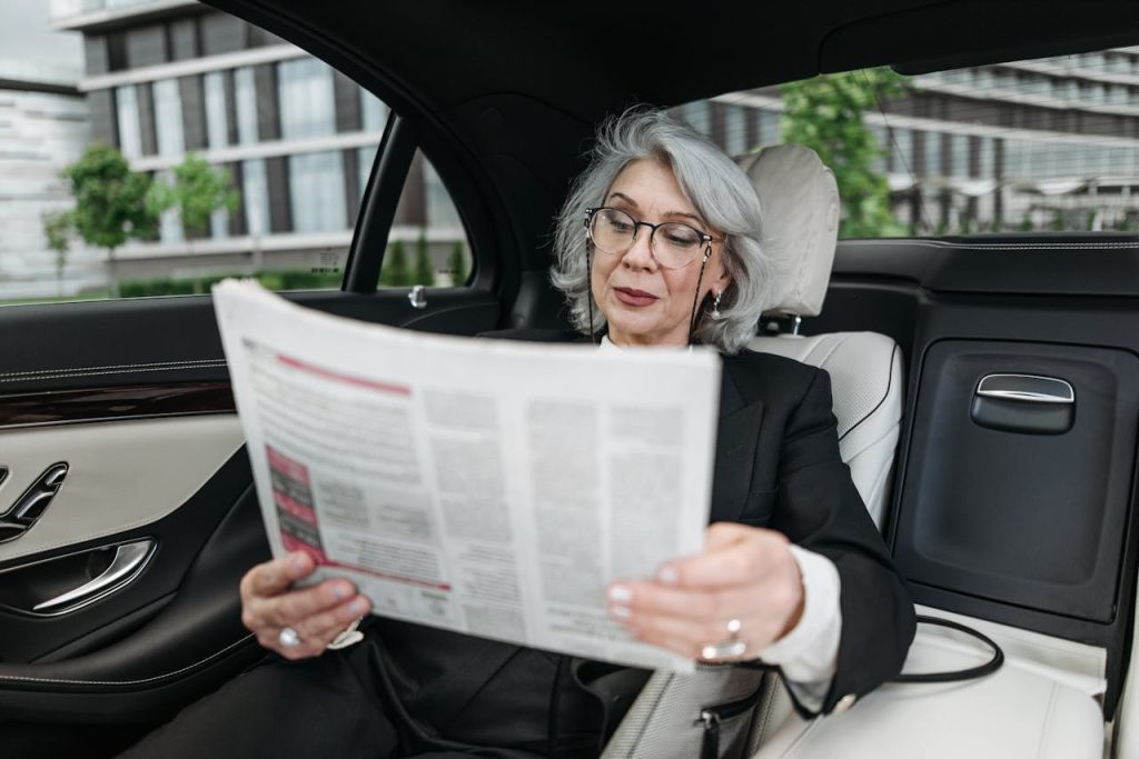 Senior woman reading a newspaper inside a modern car, capturing a serene moment.