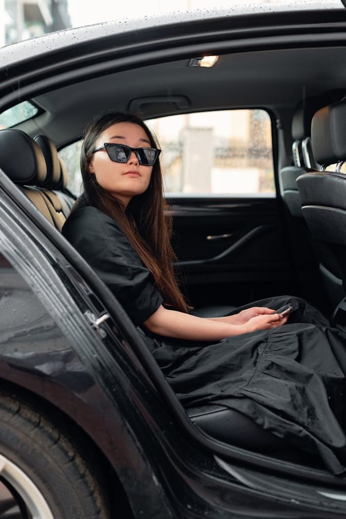 Asian woman sitting in car seat wearing sunglasses, exuding confidence and style.