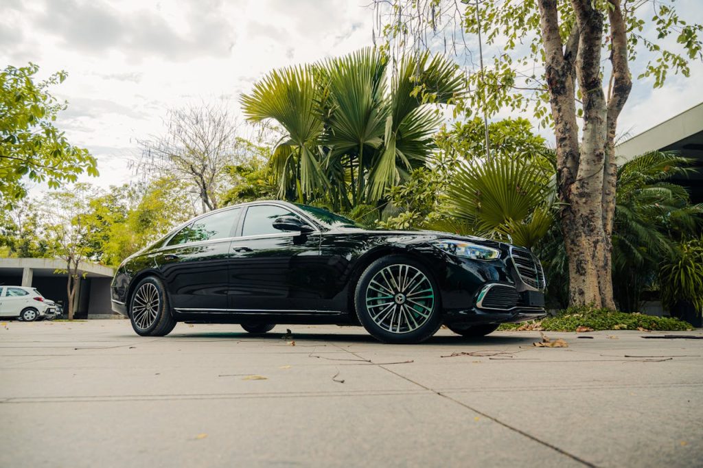 A luxurious black sedan parked outdoors amidst lush tropical greenery.